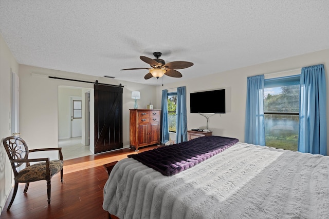 bedroom with hardwood / wood-style floors, ceiling fan, a barn door, and a textured ceiling