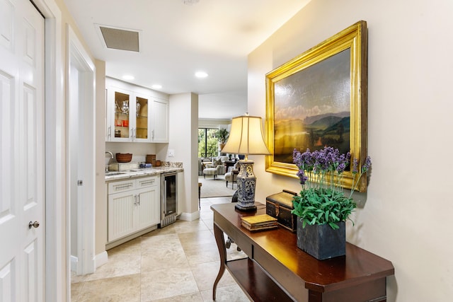 kitchen with white cabinets, light stone counters, sink, and beverage cooler