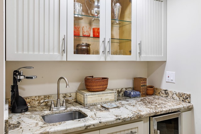 bar featuring white cabinets, light stone counters, sink, and beverage cooler