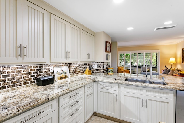 kitchen with kitchen peninsula, decorative backsplash, sink, and light stone counters