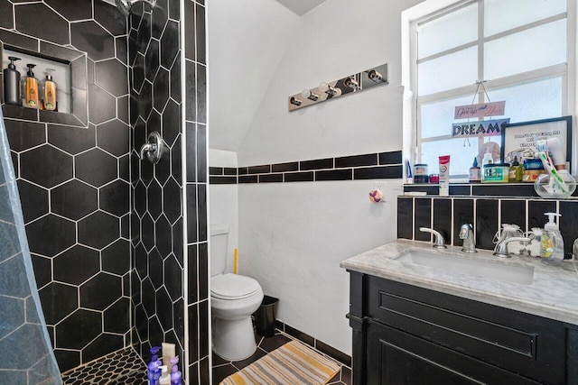 bathroom featuring vanity, toilet, tiled shower, and vaulted ceiling