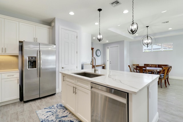 kitchen with white cabinetry, sink, hanging light fixtures, stainless steel appliances, and an island with sink