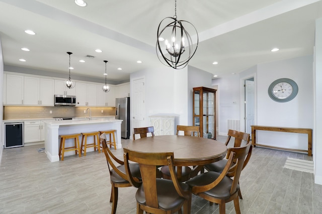 dining area featuring a chandelier, light hardwood / wood-style flooring, beverage cooler, and sink