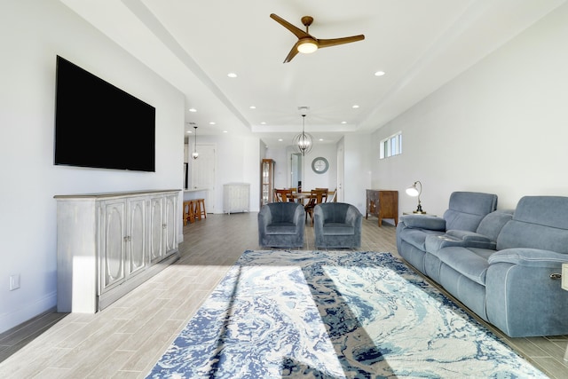 living room featuring ceiling fan with notable chandelier and a tray ceiling