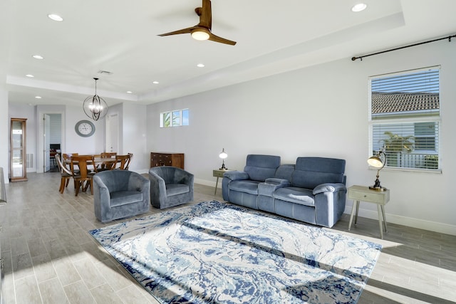 living room featuring ceiling fan with notable chandelier and a raised ceiling