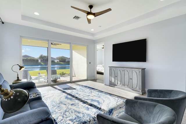 living room featuring light hardwood / wood-style flooring, a raised ceiling, and ceiling fan