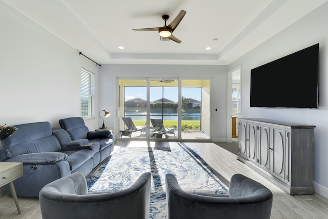 living area featuring a tray ceiling, recessed lighting, a ceiling fan, wood tiled floor, and baseboards