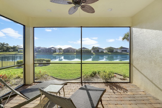 sunroom with a ceiling fan and a water view