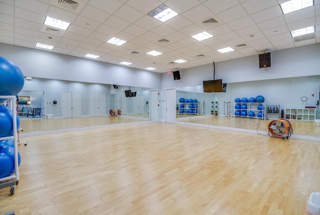 exercise area with a drop ceiling, light hardwood / wood-style floors, and a high ceiling