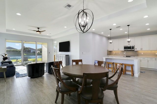 dining space featuring light wood-style flooring, a raised ceiling, and visible vents