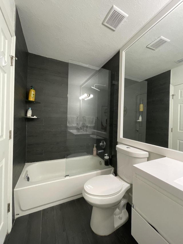 full bathroom with vanity, tiled shower / bath combo, a textured ceiling, and toilet