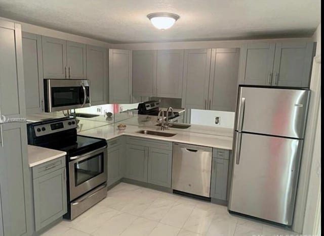 kitchen with a textured ceiling, stainless steel appliances, gray cabinetry, and sink