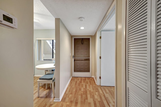 hall with a textured ceiling and light wood-type flooring