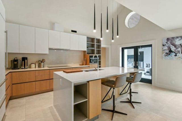 kitchen with a kitchen island with sink, sink, black electric cooktop, light tile patterned flooring, and white cabinetry