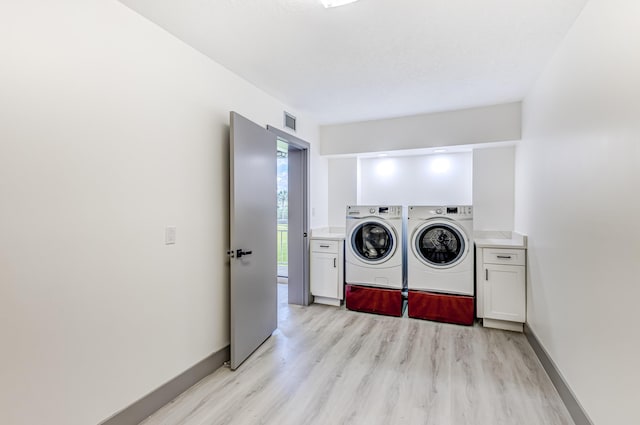 clothes washing area featuring washer and clothes dryer, cabinets, and light wood-type flooring