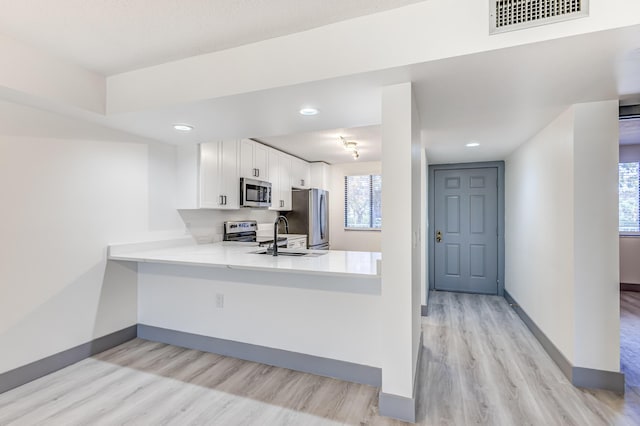 kitchen with white cabinetry, sink, stainless steel appliances, light hardwood / wood-style flooring, and kitchen peninsula