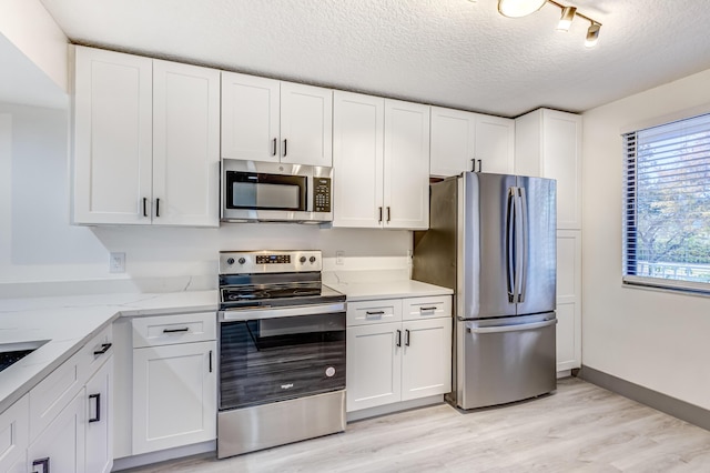 kitchen with appliances with stainless steel finishes, a textured ceiling, light hardwood / wood-style flooring, and white cabinetry