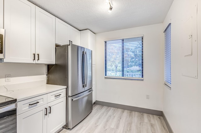 kitchen with light stone counters, appliances with stainless steel finishes, a textured ceiling, white cabinets, and light wood-type flooring