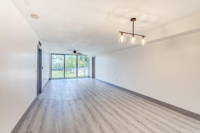 empty room with ceiling fan, floor to ceiling windows, a textured ceiling, and light hardwood / wood-style flooring