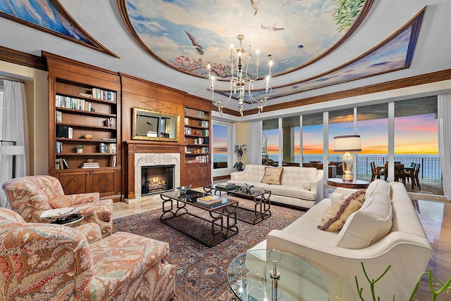 living area with a notable chandelier, a premium fireplace, built in features, a raised ceiling, and crown molding