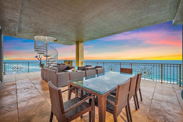 patio terrace at dusk featuring outdoor dining area and a water view