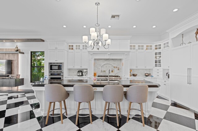 kitchen featuring backsplash, crown molding, a center island with sink, white cabinets, and appliances with stainless steel finishes