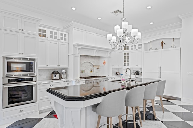 kitchen featuring ornamental molding, stainless steel appliances, a kitchen island with sink, sink, and white cabinetry