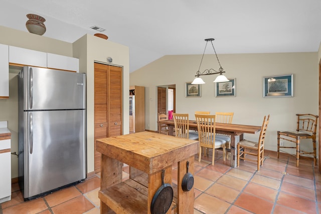 kitchen featuring lofted ceiling, white cabinets, hanging light fixtures, stainless steel fridge, and light tile patterned floors