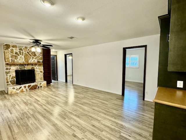 unfurnished living room featuring a stone fireplace, ceiling fan, wood-type flooring, and a textured ceiling