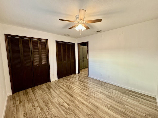 unfurnished bedroom featuring ceiling fan, multiple closets, and light hardwood / wood-style flooring