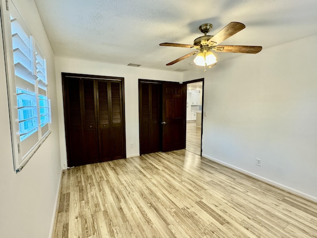 unfurnished bedroom with a textured ceiling, ceiling fan, two closets, and light wood-type flooring