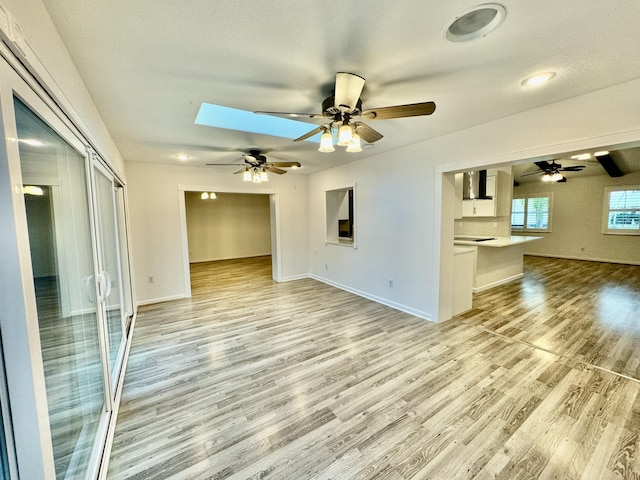 unfurnished living room featuring a skylight, ceiling fan, a textured ceiling, and light wood-type flooring