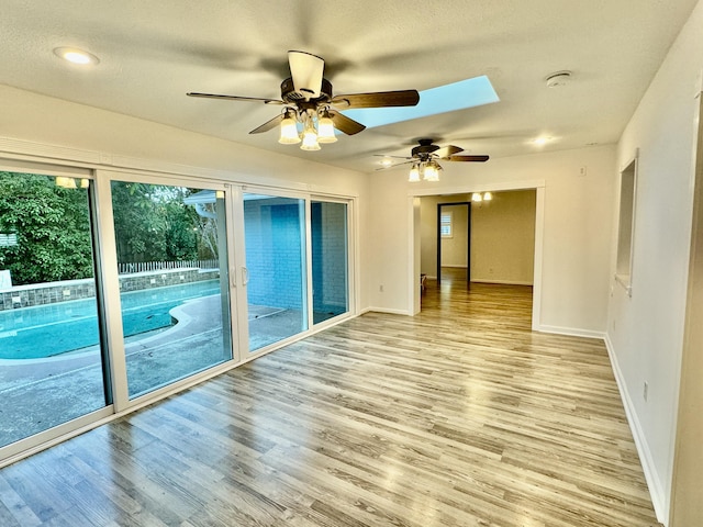 spare room with ceiling fan, light hardwood / wood-style floors, a textured ceiling, and a skylight