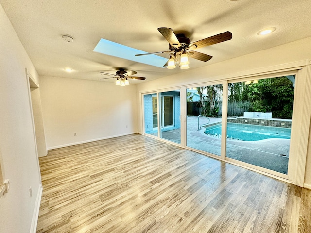 interior space featuring a skylight, ceiling fan, a textured ceiling, and light wood-type flooring