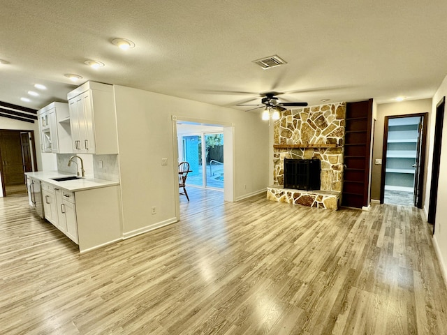 living room with ceiling fan, sink, a stone fireplace, a textured ceiling, and light wood-type flooring