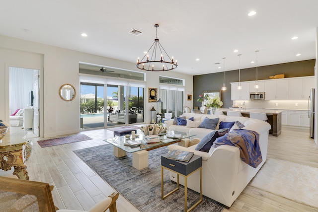 living room featuring ceiling fan with notable chandelier and light hardwood / wood-style flooring