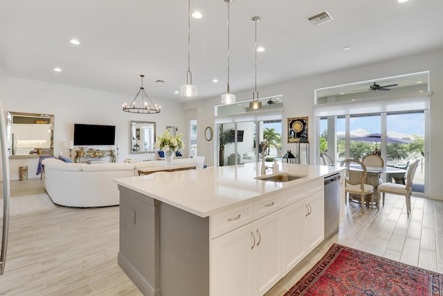 kitchen with sink, dishwasher, a kitchen island with sink, hanging light fixtures, and white cabinetry