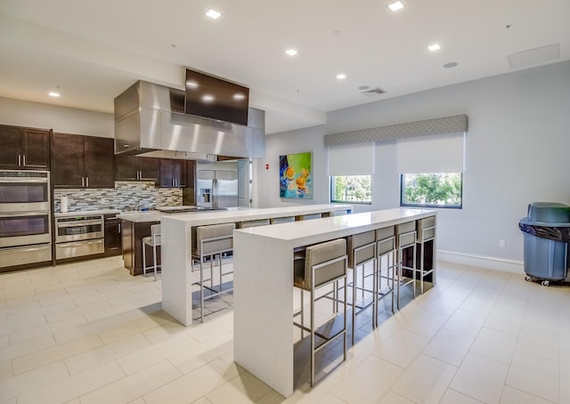 kitchen with appliances with stainless steel finishes, island range hood, a kitchen island, and a breakfast bar area