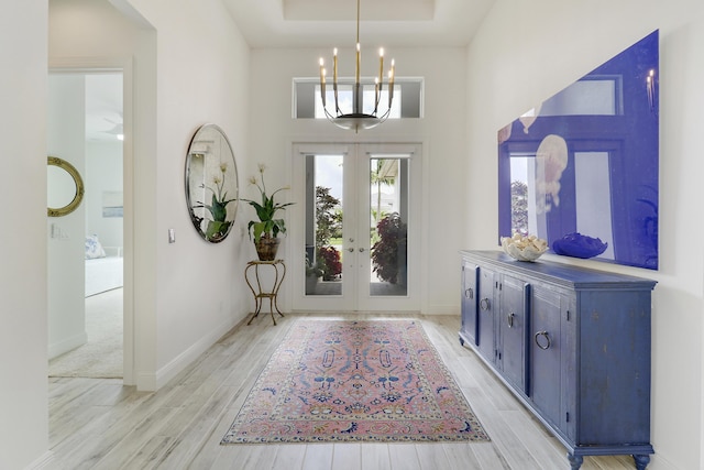 entryway featuring french doors, light wood-type flooring, a tray ceiling, a notable chandelier, and a towering ceiling