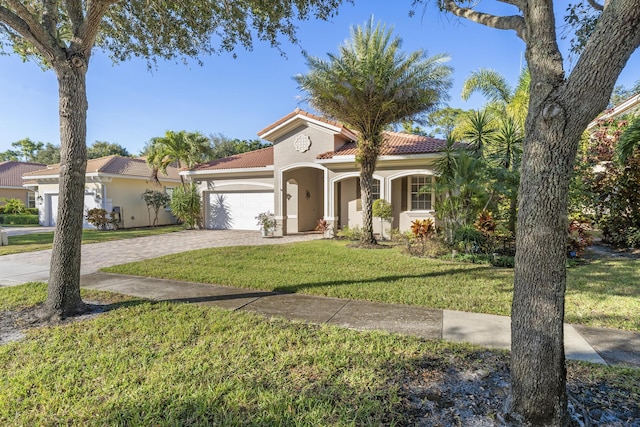 mediterranean / spanish-style house with a tiled roof, an attached garage, decorative driveway, a front yard, and stucco siding