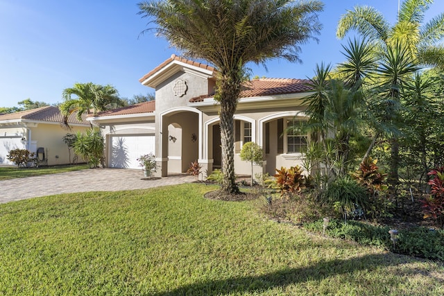 mediterranean / spanish home with an attached garage, a tiled roof, decorative driveway, stucco siding, and a front lawn