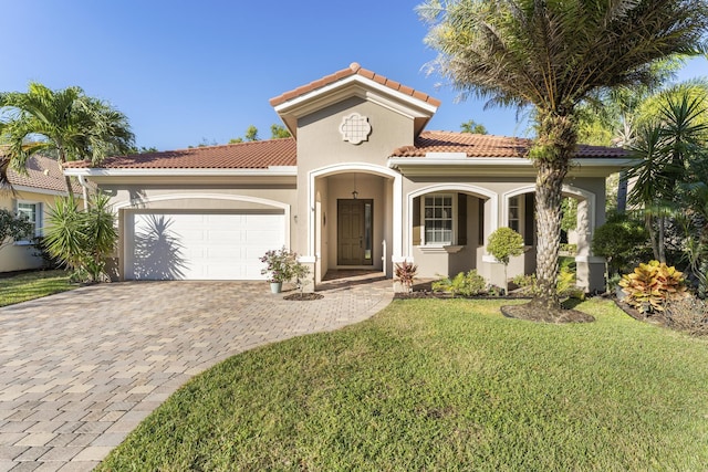 mediterranean / spanish house featuring decorative driveway, stucco siding, a garage, a tiled roof, and a front lawn