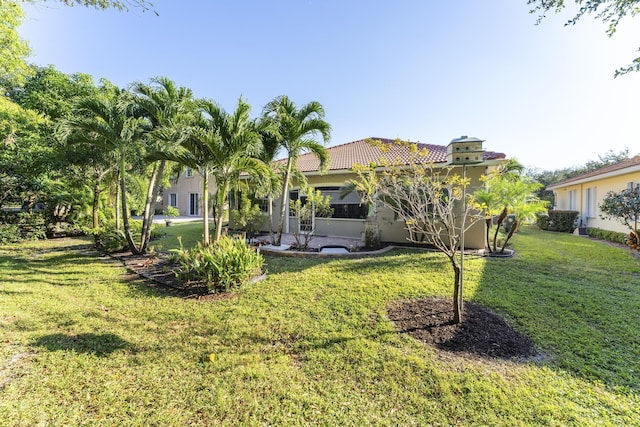 rear view of property with a yard, a tile roof, and stucco siding