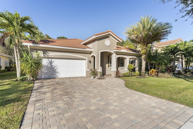 mediterranean / spanish house with decorative driveway, stucco siding, a front yard, a garage, and a tiled roof