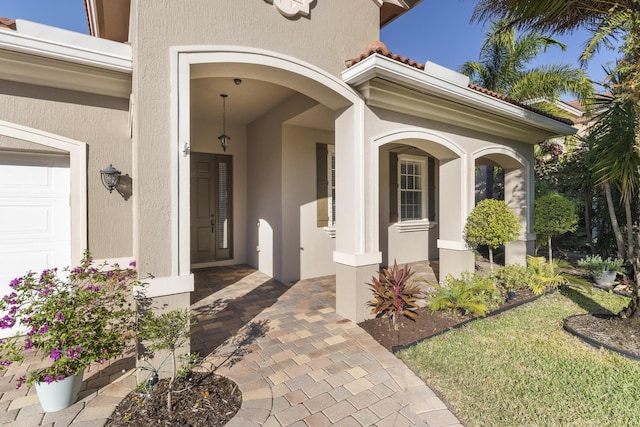 view of exterior entry with an attached garage and stucco siding