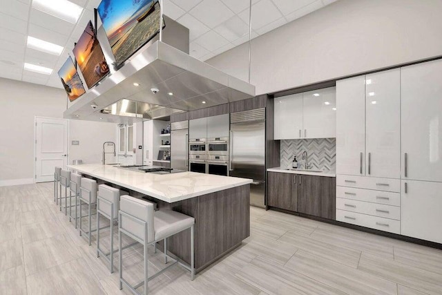 kitchen featuring a breakfast bar, ventilation hood, a spacious island, white cabinetry, and stainless steel appliances