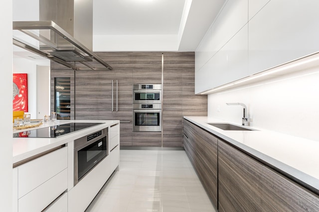 kitchen with island exhaust hood, appliances with stainless steel finishes, sink, light tile patterned floors, and white cabinetry