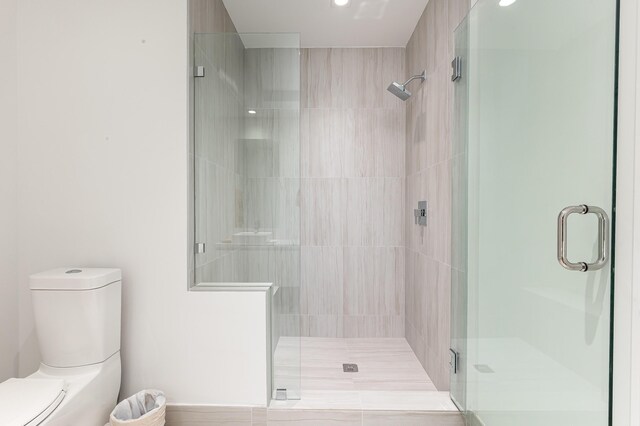 bathroom featuring a shower with door and toilet