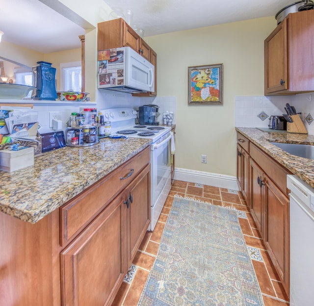 kitchen with tasteful backsplash, light stone counters, sink, and white appliances