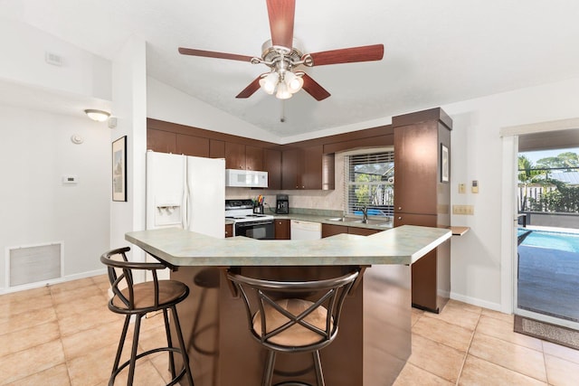 kitchen with white appliances, a kitchen breakfast bar, vaulted ceiling, dark brown cabinets, and light tile patterned flooring